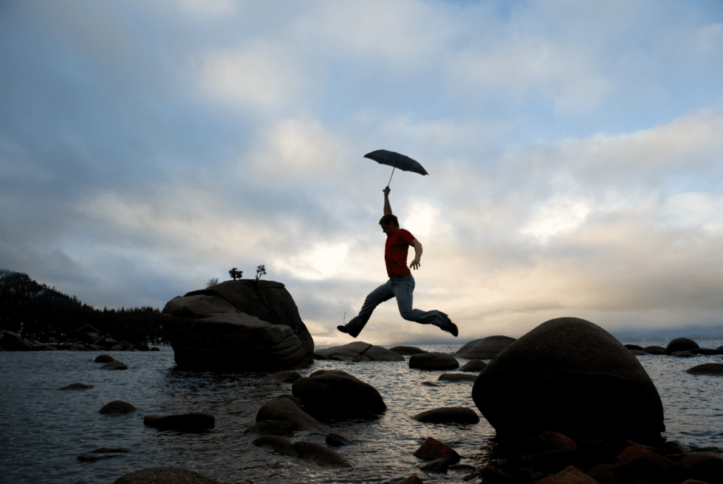 person leaping over rocks with an umbrella