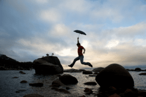 person leaping over rocks with an umbrella