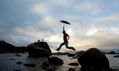 person leaping over rocks with an umbrella