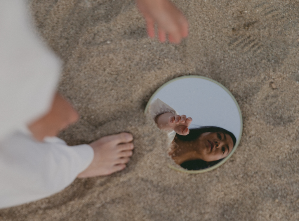 woman pointing to a reflection of herself in a mirror on a beach